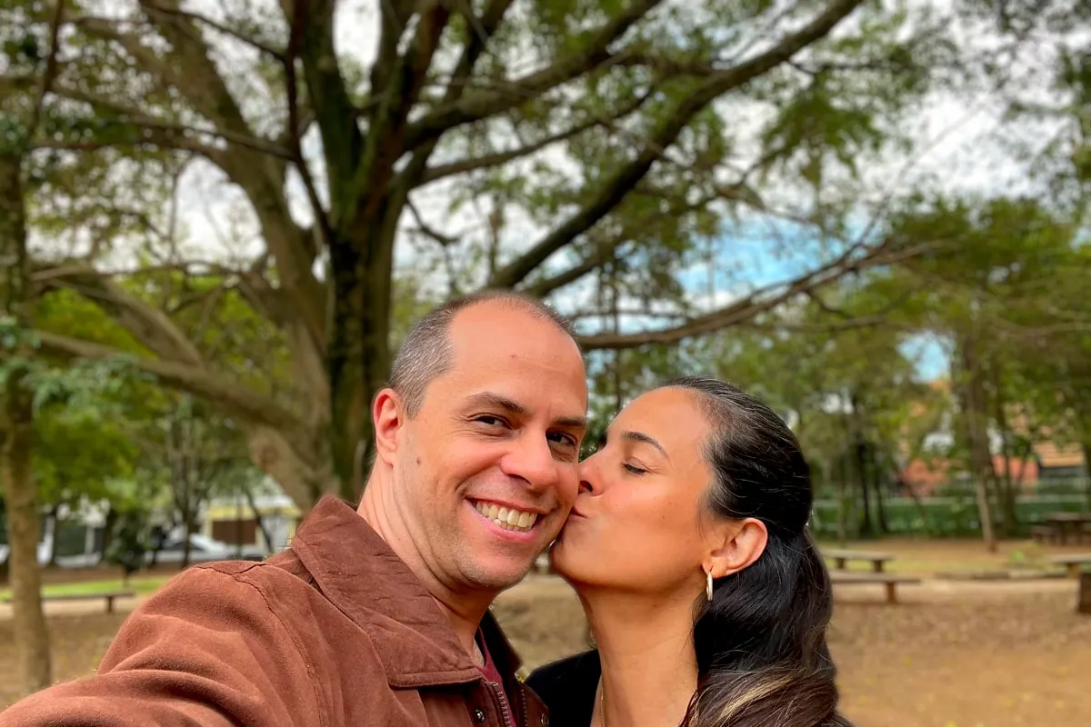 Michelle beijando o rosto do Adriano, debaixo de uma árvore